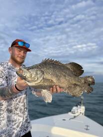 Angler proudly displaying a large Barramundi while fishing on a boat in open waters.
