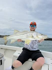 A young angler proudly displaying a large Snook while fishing on a boat, showcasing a successful day on the water.