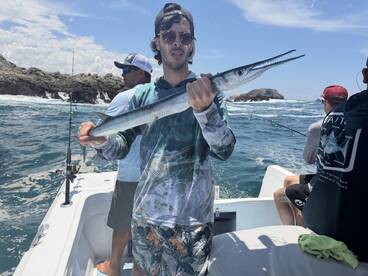 Angler proudly displaying a Barracuda while fishing on a boat in a coastal environment, surrounded by friends.