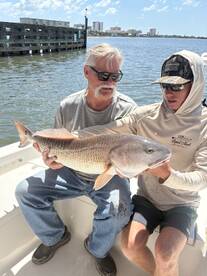 Two anglers proudly displaying a large Redfish on a boat, enjoying a sunny day on the water.