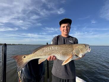 A young angler proudly displaying a large Redfish while fishing on a sunny day.
