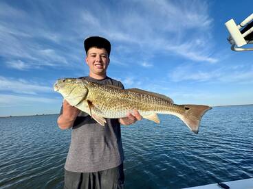 A young angler proudly displaying a large Redfish while fishing in calm waters.
