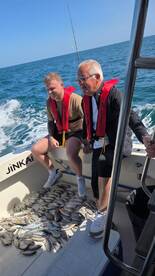 Two anglers enjoying their catch on a boat, surrounded by a variety of fish after a successful fishing trip.