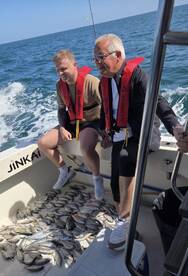 Two anglers enjoying their catch on a boat, surrounded by a variety of fish after a successful fishing trip.