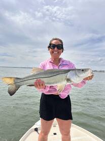 Angler proudly displaying a large Snook while standing on the boat, enjoying a sunny day on the water.
