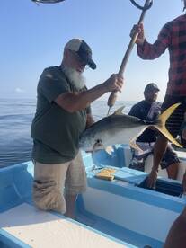 An angler proudly displaying a large Jack Crevalle while fishing on a small boat in calm waters.