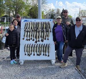 A family poses proudly in front of a catch board displaying a successful haul of Walleye after a fishing trip.