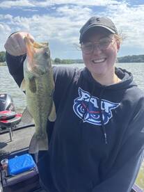 A proud angler holding a large Largemouth Bass while fishing on a serene lake, showcasing a successful day on the water.