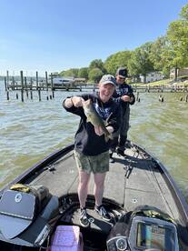 A happy angler proudly displaying a large bass while fishing on a lake, with another person in the background enjoying the day.