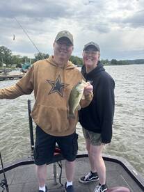 A couple proudly displaying a large Largemouth Bass while fishing on a lake, showcasing a fun day on the water.