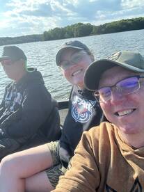 Three anglers enjoying a day on the water, smiling for a selfie while seated in a fishing boat.