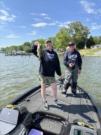 A happy angler proudly displaying a Largemouth Bass while fishing on a Ranger boat in a scenic lake setting.