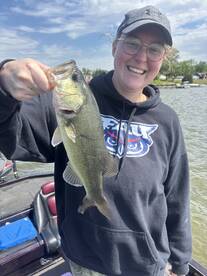 Angler proudly displaying a large Largemouth Bass while fishing from a boat on a sunny day.