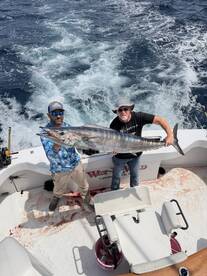 Two anglers proudly displaying a large Wahoo on a sportfishing boat, showcasing a successful deep-sea fishing trip.