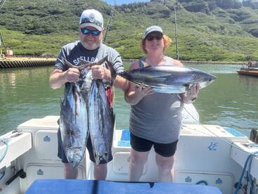 Two anglers proudly displaying their catch of Tuna while on a fishing charter in a scenic coastal environment.