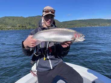 A young angler proudly displaying a large Rainbow Trout while fishing on a scenic lake.