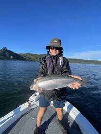 Young angler proudly displaying a Rainbow Trout while fishing on a serene lake, showcasing a beautiful day on the water.