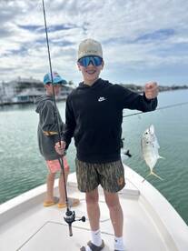 A young angler proudly displaying a small fish while fishing from a boat, with another child in the background, enjoying a day on the water.