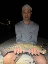 Angler proudly displaying a Speckled Trout while fishing at night from a boat.