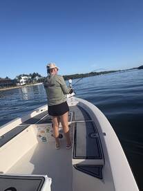 A female angler casting her line from a center console boat in calm waters, showcasing a serene fishing environment.