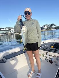 A proud angler holding a large Jack Crevalle on a boat, showcasing a successful fishing trip in a scenic waterfront setting.