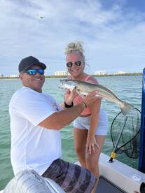 Two anglers proudly displaying a Speckled Trout while fishing in a coastal environment.
