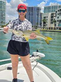Angler proudly displaying a large Snook while fishing from a boat in a vibrant urban setting.
