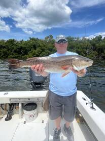 Angler proudly displaying a large Redfish while fishing in a scenic coastal environment.
