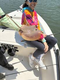 A young angler proudly displaying a stingray while fishing on a boat, showcasing a fun day on the water.
