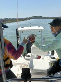 Two anglers joyfully displaying a caught fish while enjoying a day on the water, showcasing a vibrant fishing environment.