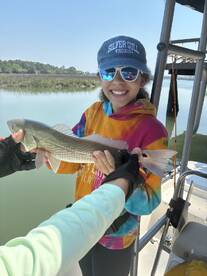 A young angler joyfully displaying a caught Redfish while fishing on a sunny day, showcasing a vibrant fishing environment.