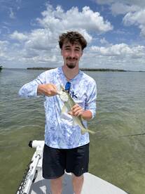 A young angler proudly displaying a Snook caught while fishing on a sunny day in a coastal waterway.
