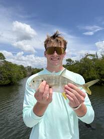 Young angler proudly displaying a small fish while fishing in a scenic waterway surrounded by mangroves.