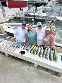 A family poses with a successful catch of Mahi Mahi and Snapper displayed on a cleaning table at the marina.