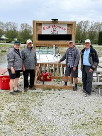A group of four anglers proudly posing with their catch of Lake Erie fish displayed on a board near their boat, showcasing a successful fishing trip.