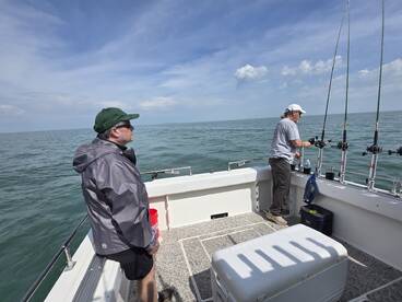 Two anglers aboard a fishing boat, one preparing to cast while the other observes the calm waters, showcasing a serene fishing experience.