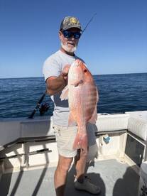 Angler proudly displaying a large Red Snapper while fishing offshore, showcasing a successful day on the water.