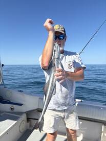 Angler proudly displaying a sleek Barracuda while fishing on a boat in clear waters.