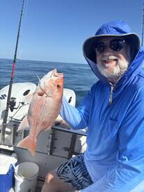 An angler proudly displaying a freshly caught Red Snapper while fishing offshore, showcasing a sunny day on the water.