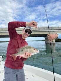 Angler displaying a vibrant Snapper while fishing near a bridge, showcasing a successful day on the water.