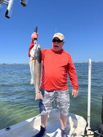 An excited angler proudly displaying a large Redfish while fishing from a boat in clear waters.
