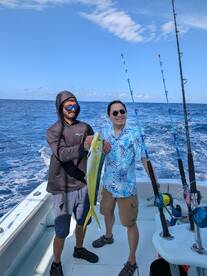 Two anglers proudly displaying a vibrant Mahi Mahi while fishing offshore, showcasing a sunny day on the water.