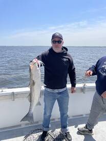 Angler proudly displaying a large Striped Bass while fishing on a charter boat.