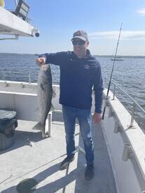 Angler proudly displaying a large Striped Bass while fishing on a charter boat.