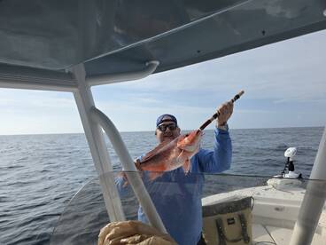 Angler proudly displaying a large Red Snapper while fishing offshore, showcasing a successful day on the water.