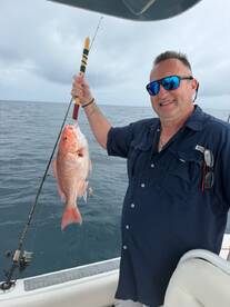 Angler proudly displaying a large Red Snapper while fishing offshore, showcasing a successful day on the water.