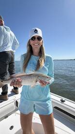 A smiling angler proudly displaying a Redfish while fishing on a sunny day.
