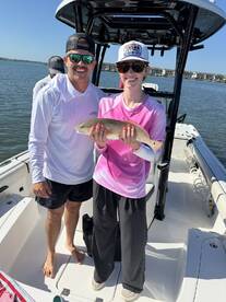 Two anglers proudly displaying a Redfish on a sunny day aboard a fishing boat.