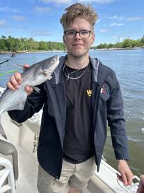 Angler proudly displaying a freshly caught catfish while on a boat, showcasing a successful fishing trip.