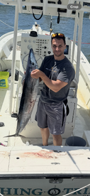 Angler proudly displaying a large Wahoo on a fishing boat, showcasing a successful day on the water.